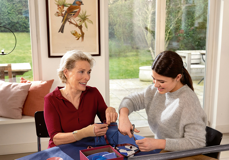 Young woman helps an older woman wearing a wrist support to wrap a gift Young woman helps an older woman wearing a wrist support to wrap a gift